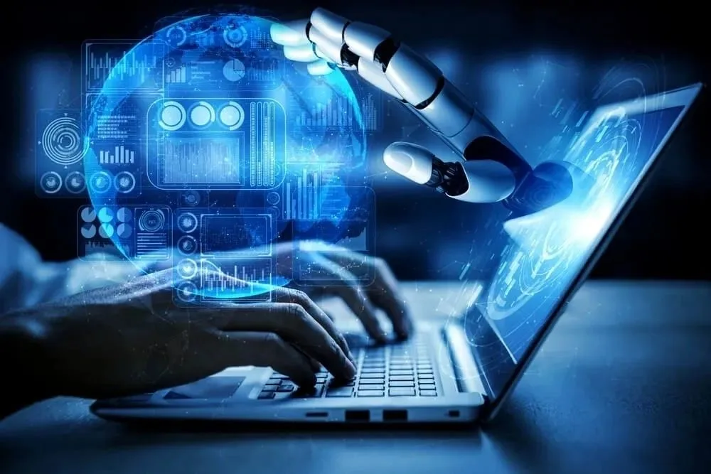 A robotic hand interacts with a laptop displaying futuristic data visualizations.
